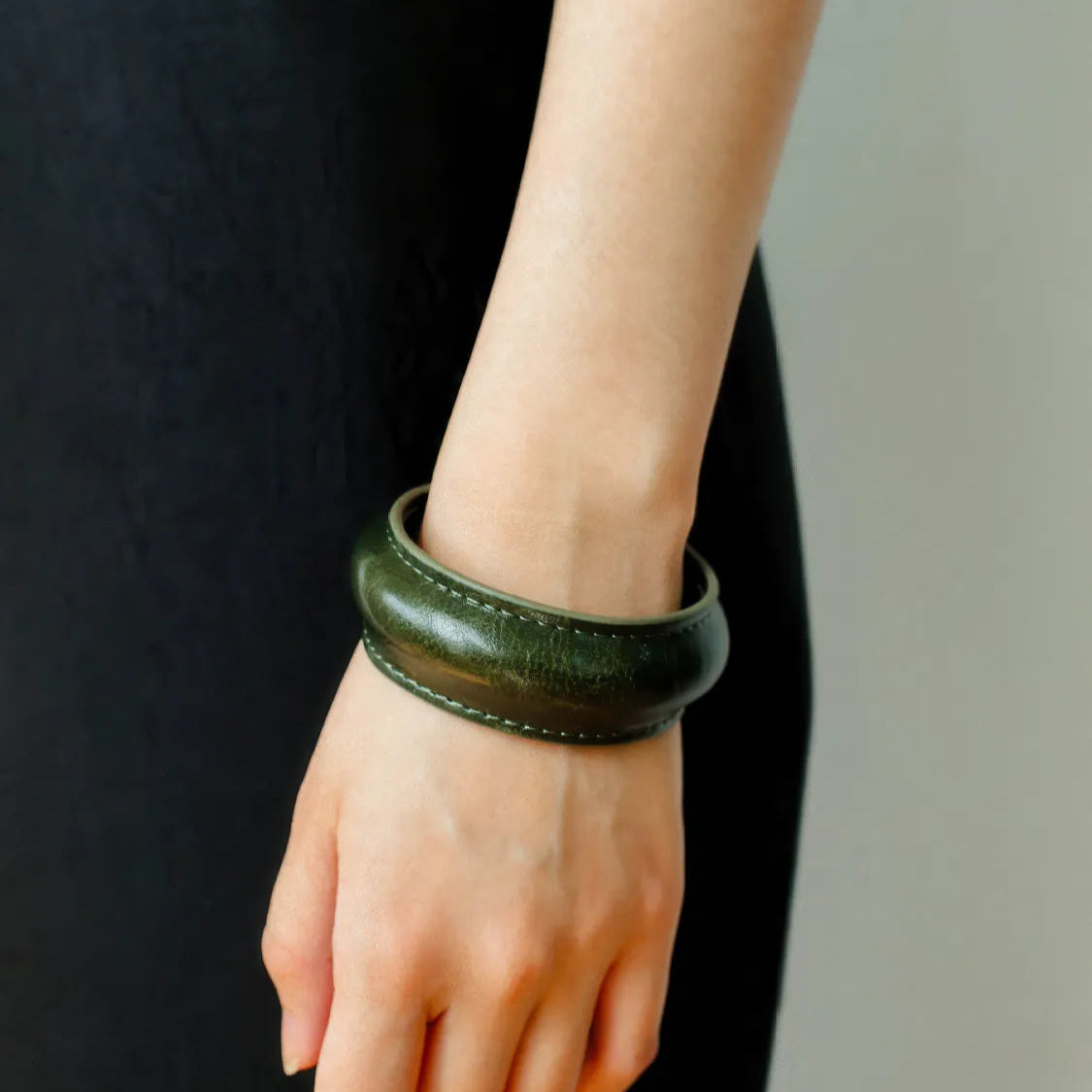 Hand wearing a green leather bracelet against a black background
