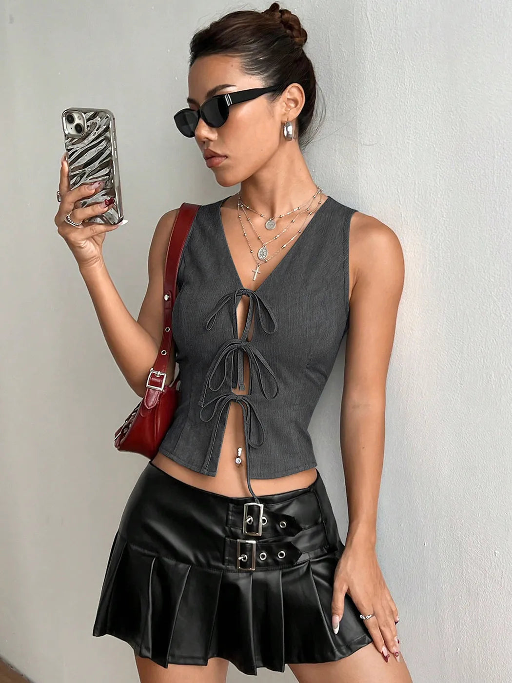 Woman in a gray top and black skirt holding a phone with a zebra case against a plain background #Color_DarkGray