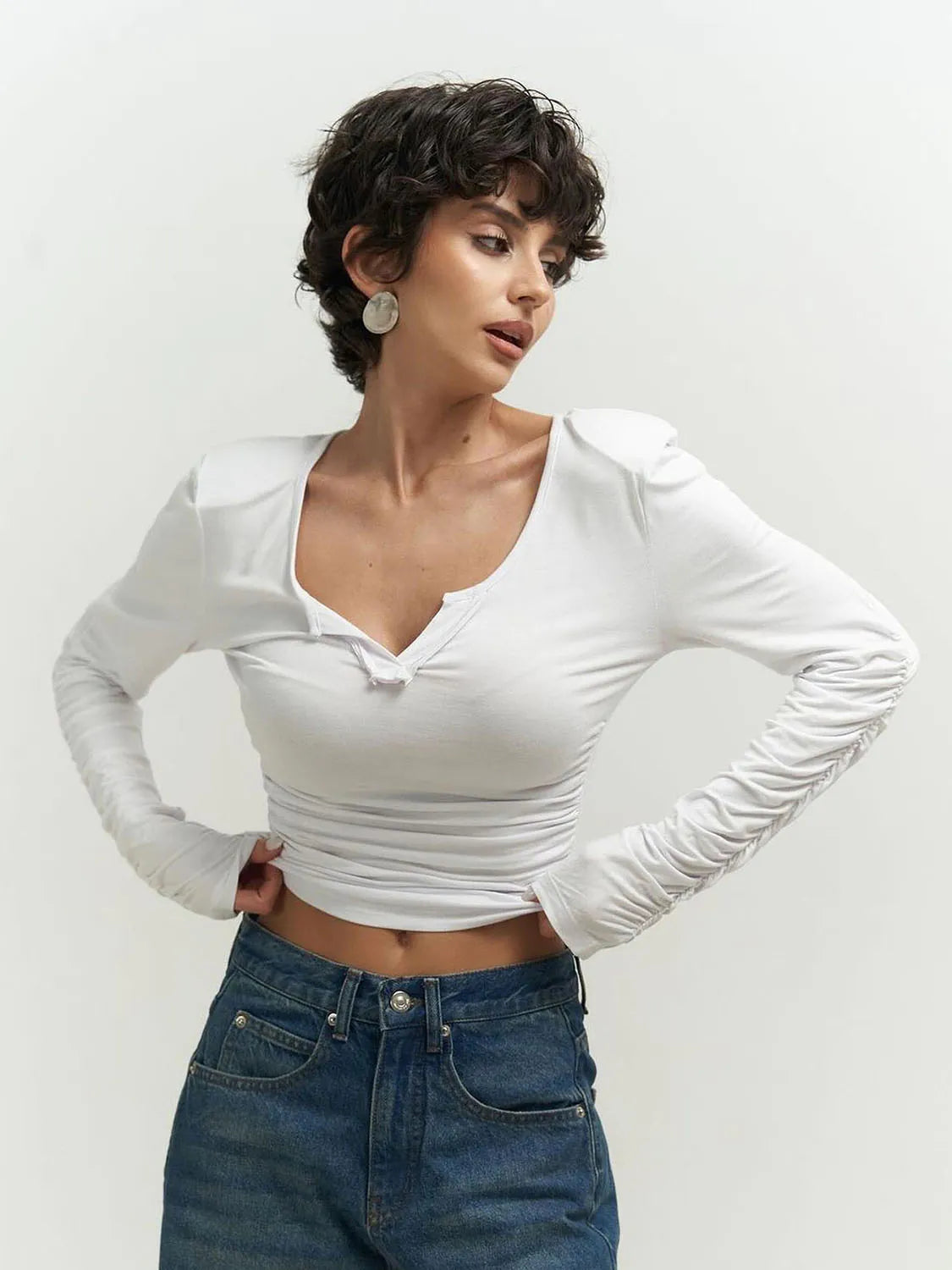 Woman wearing a white long-sleeve top and blue jeans against a plain background. #Color_White