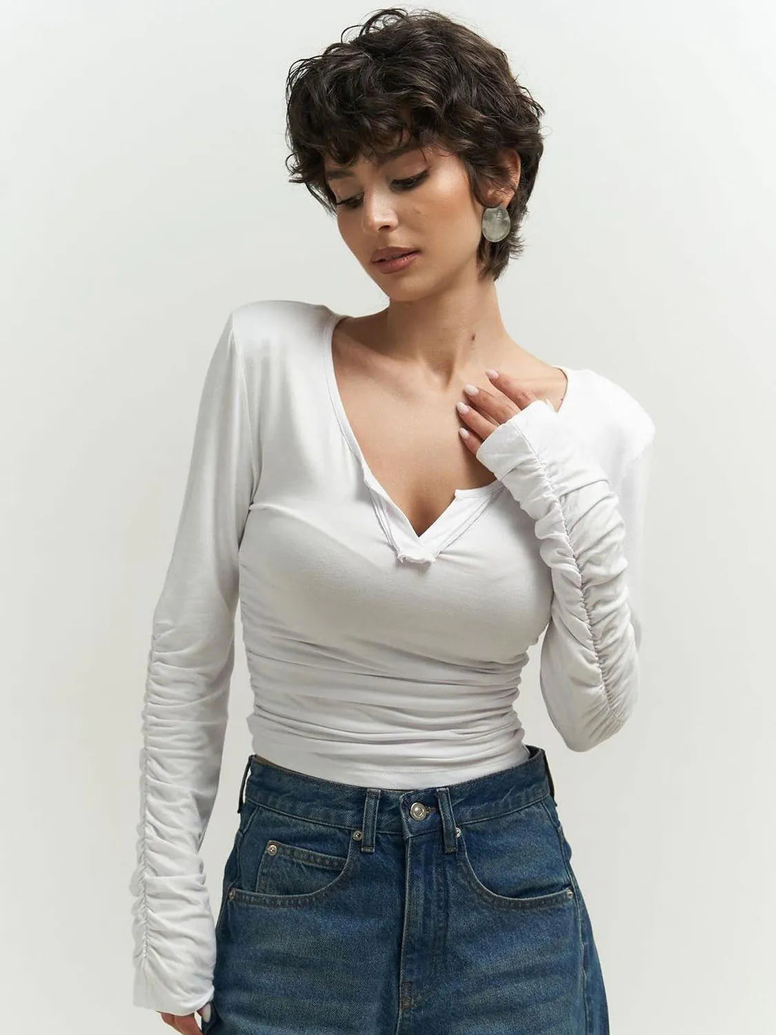 Woman wearing a white long-sleeve top and blue jeans against a plain background. #Color_White