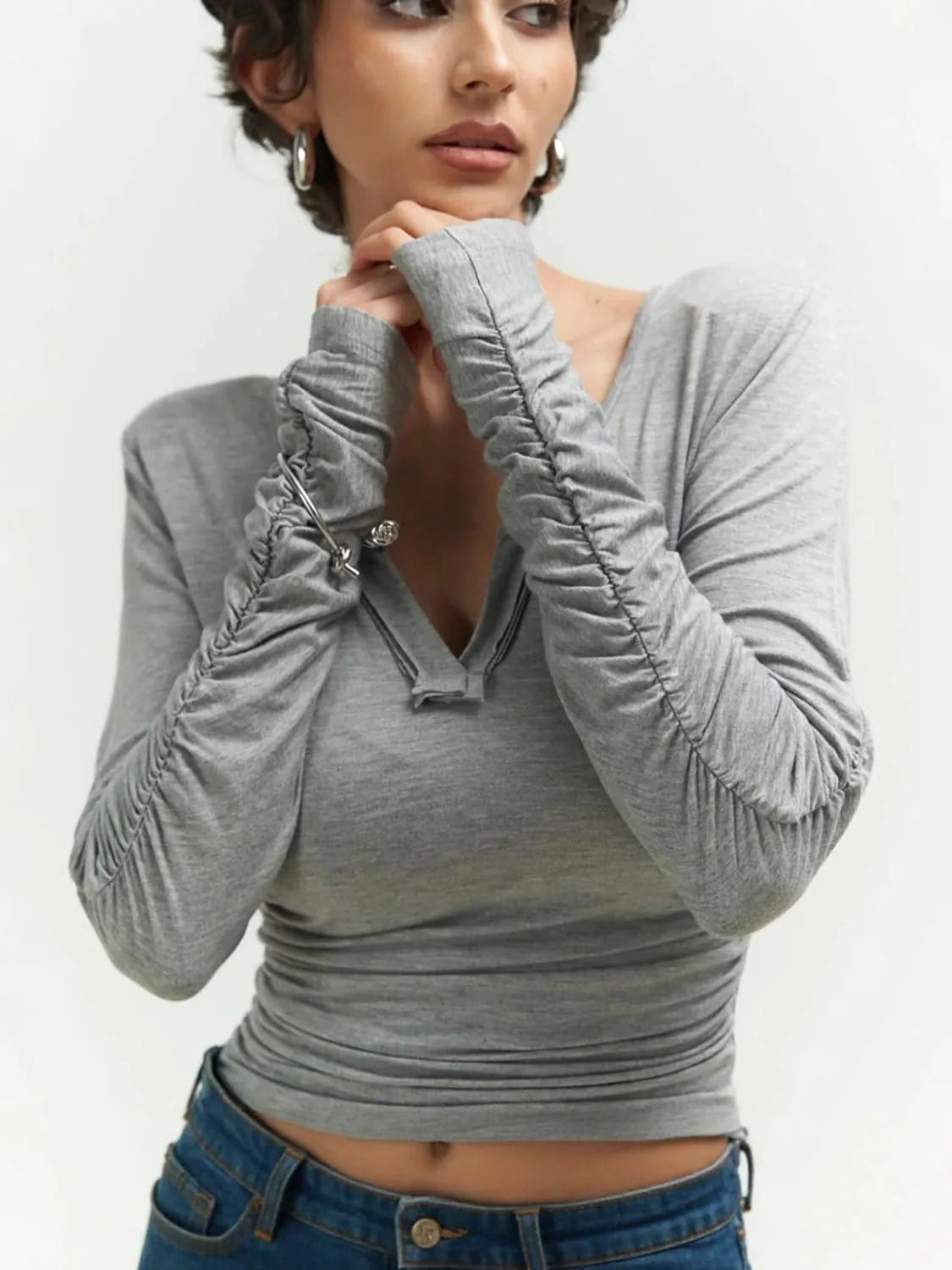 Woman wearing a gray long-sleeve top with ruched shoulders against a white background. #Color_Gray