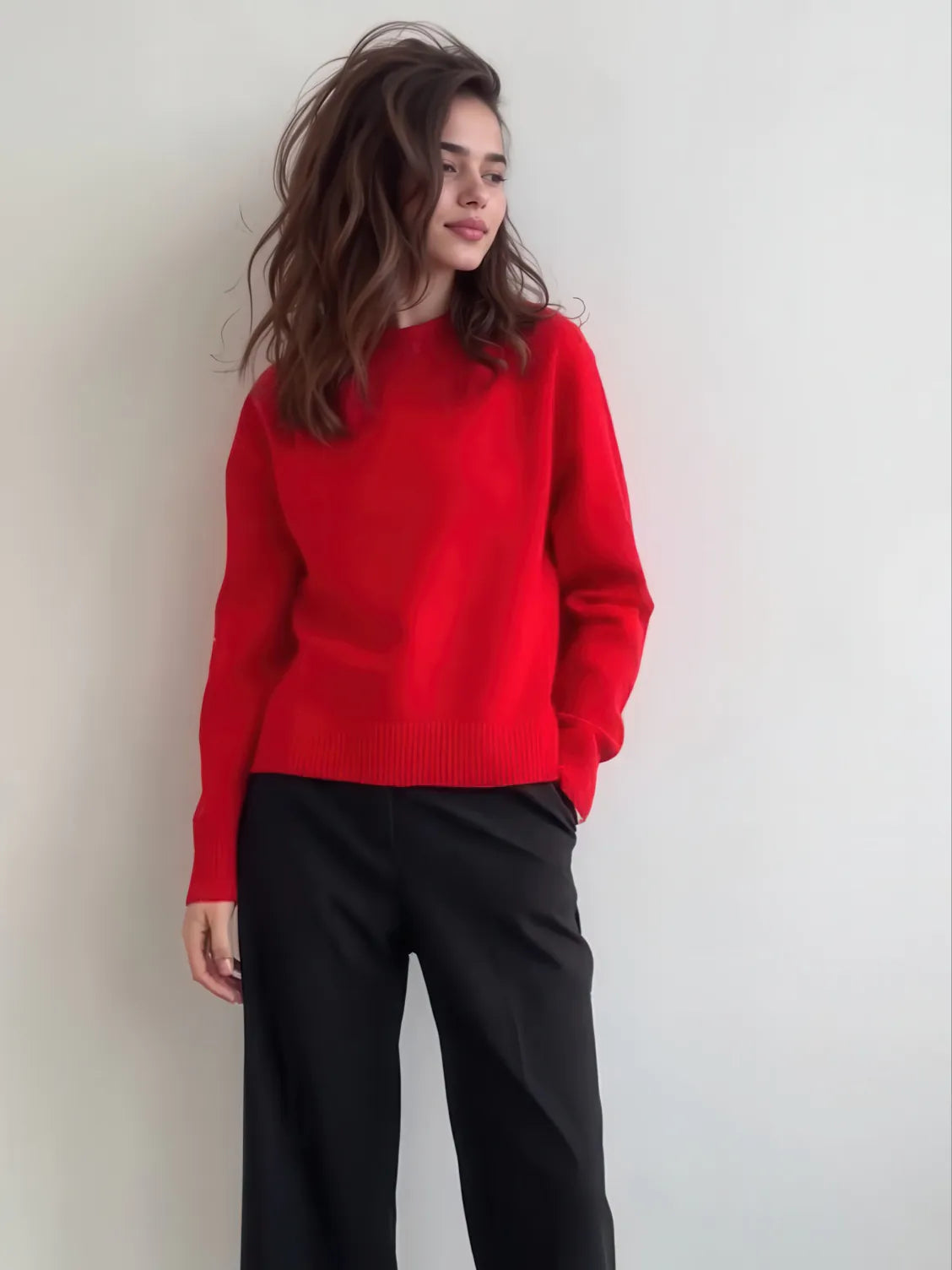 Person wearing a red sweater and black pants against a plain background. #Color_Red
