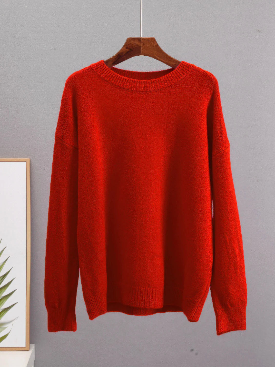 Red sweater on a wooden hanger against a gray background. #Color_Red