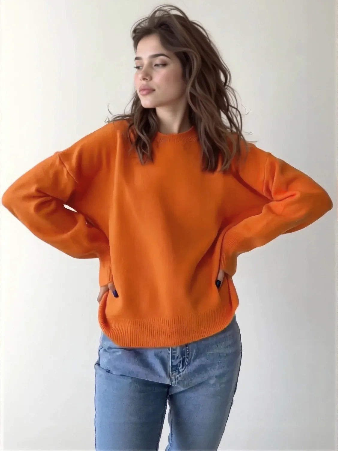 Woman wearing an orange sweater and blue jeans against a white background. #Color_Orange