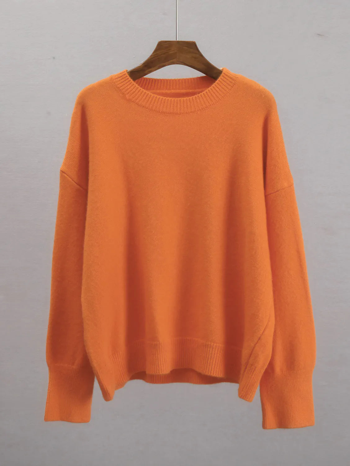 Orange sweater on a wooden hanger against a gray background. #Color_Orange