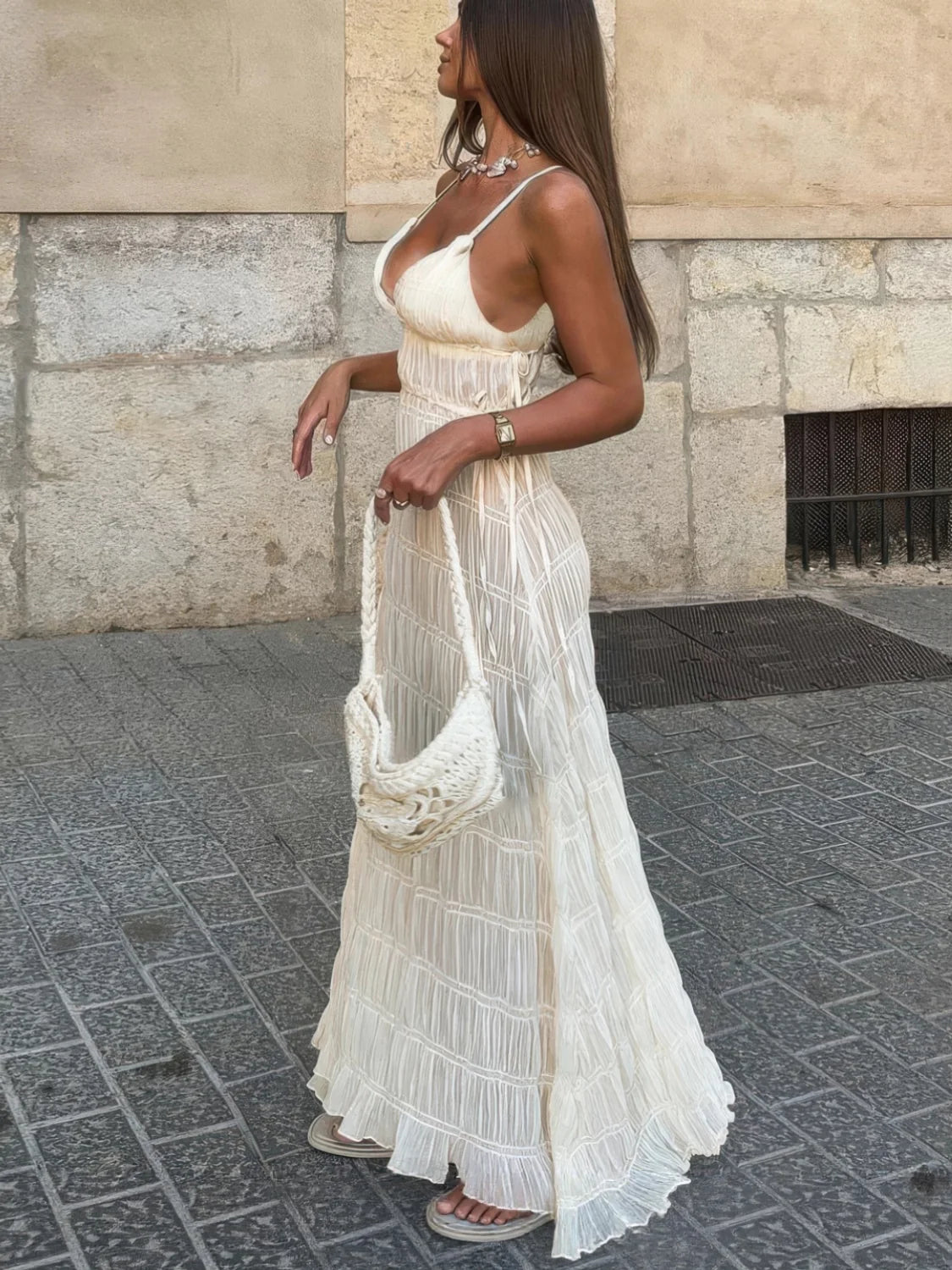 Woman in a long, light-colored dress standing on a street.