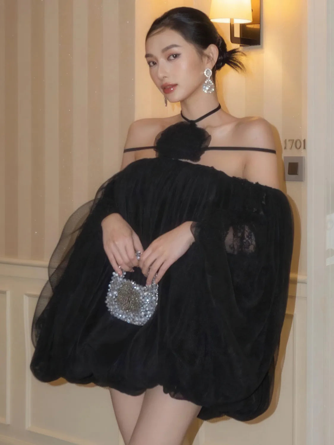 Woman in a black dress holding a silver clutch indoors. #Color_Black