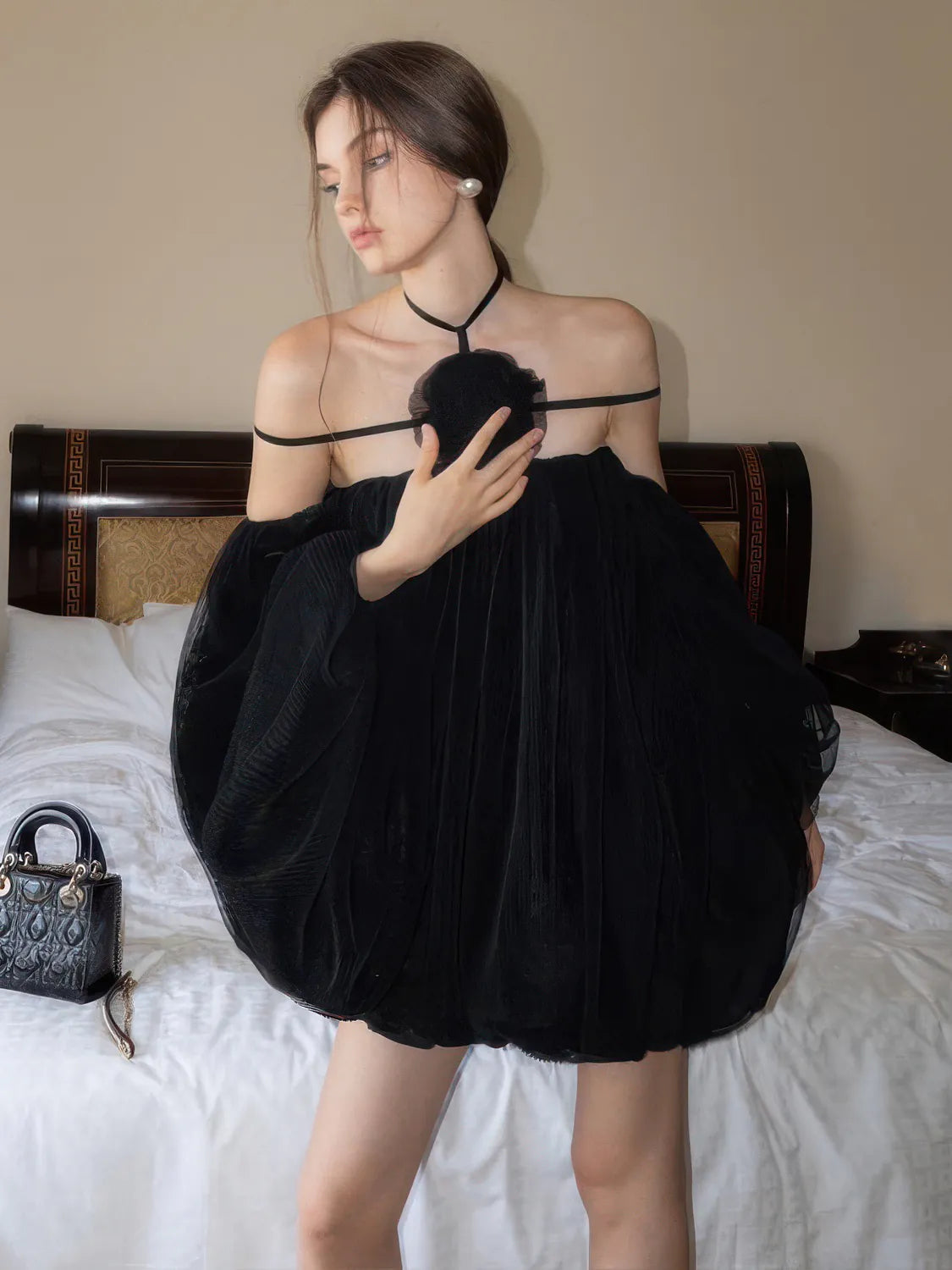 Woman holding a black dress in a bedroom setting. #Color_Black