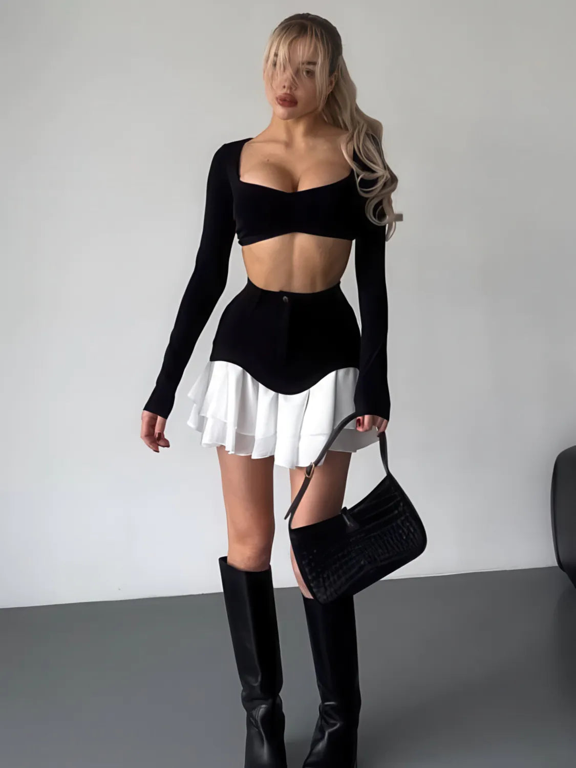 Woman wearing a black long-sleeve top and white skirt with black knee-high boots against a plain background. #Color_Black