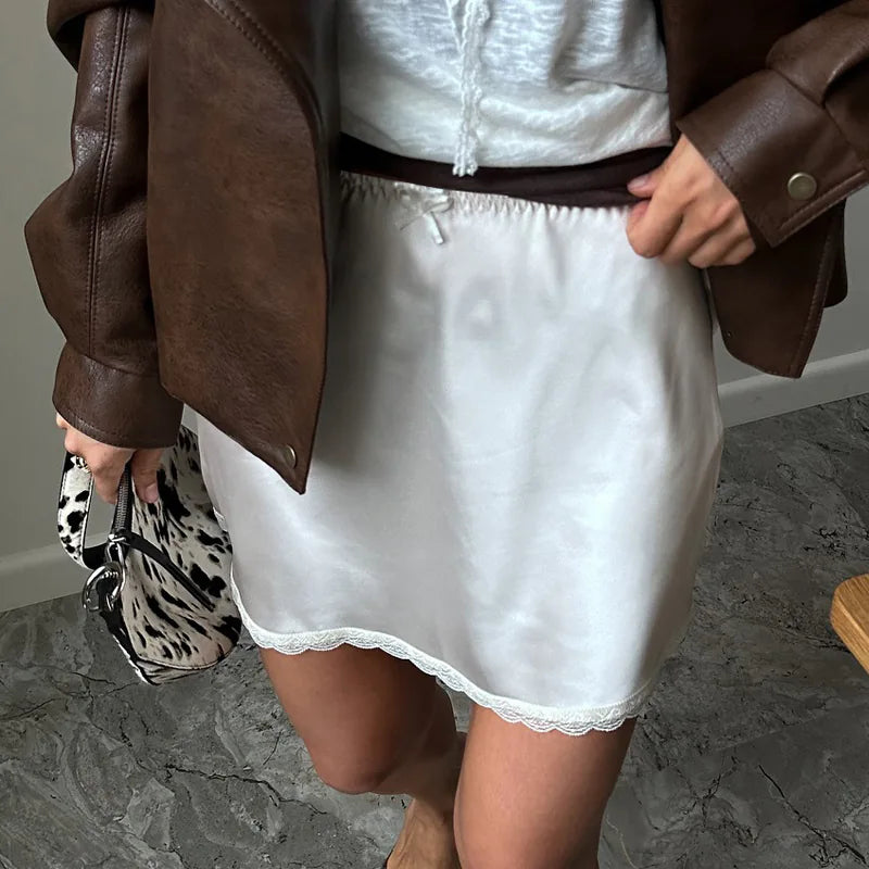 Person wearing a white dress with a brown leather jacket and holding a patterned bag. #Color_White