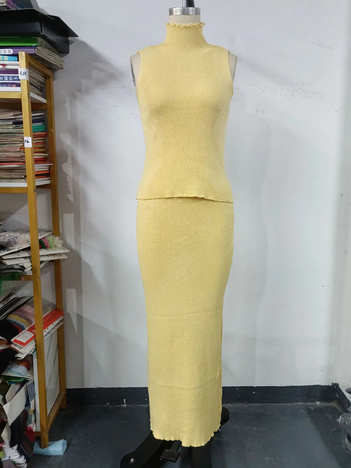 Mannequin wearing a yellow outfit against a white wall with a bookshelf in the background. #Color_Yellow