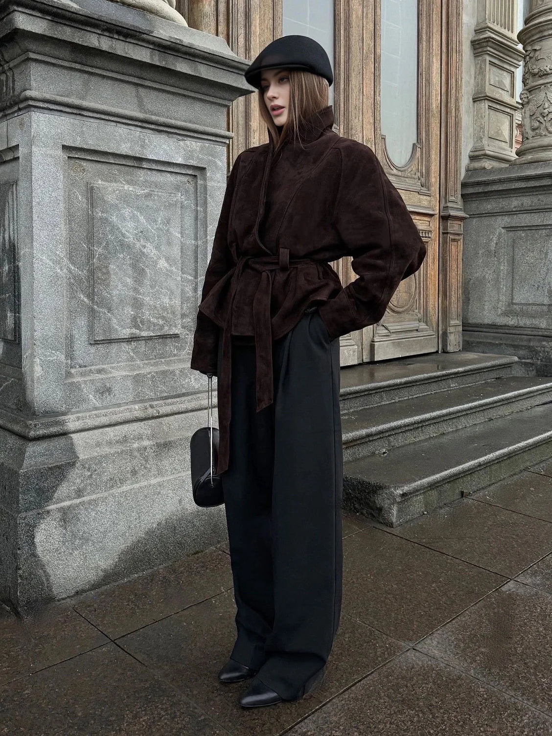 Woman in a brown coat and black hat standing in front of classical architecture. #Color_Brown